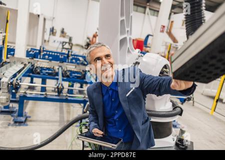 Smiling mature engineer with tablet PC touching robotic arm Stock Photo