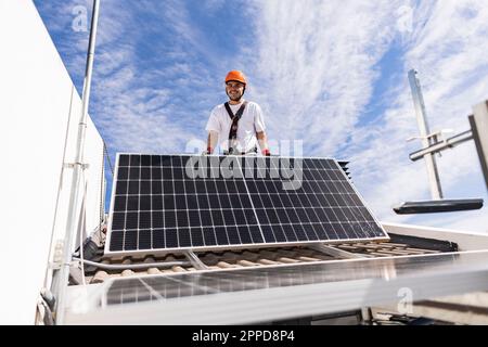 Smiling young engineer installing solar panels on roof Stock Photo