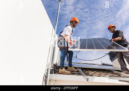 Young technician with colleague installing solar panels on roof Stock Photo