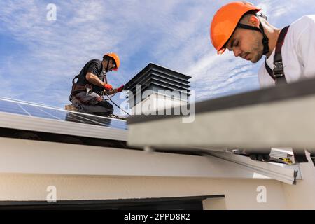 Young engineer wearing hardhat installing solar panels with colleague Stock Photo