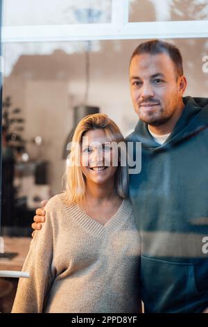 Couple standing with arm around seen through glass Stock Photo