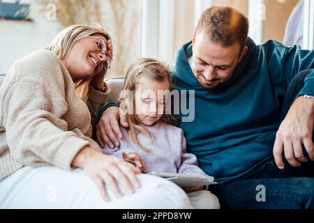Father looking at girl using tablet PC by mother at home Stock Photo