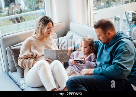 Parents sharing ultrasound scan with daughter sitting on sofa at home Stock Photo