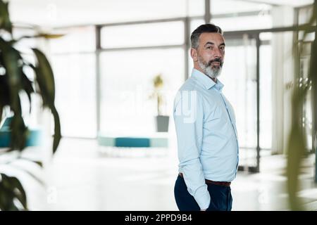 Confident businessman standing with hands in pockets in office Stock Photo
