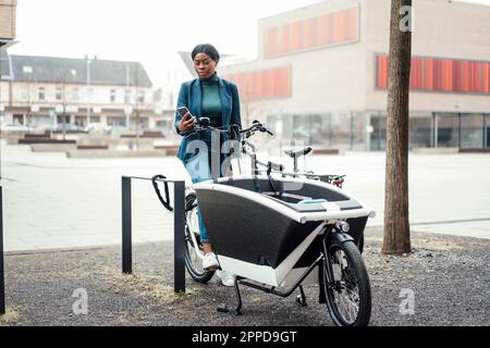 Businesswoman surfing net through smart phone sitting on cargo bike Stock Photo