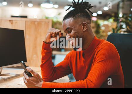 Excited businessman looking at smart phone cheering in office Stock Photo
