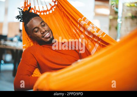 Smiling young businessman relaxing in hammock in office Stock Photo