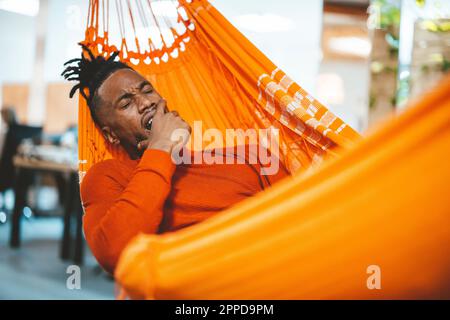 Tired businessman lying in hammock and yawning in office Stock Photo