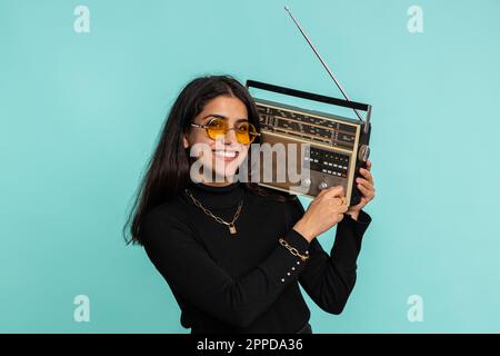 Indian woman using retro tape record player to listen music, disco dancing of favorite track, having fun, entertaining, fan of vintage technologies. Pretty hindu girl isolated on blue background Stock Photo