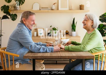 Affectionate senior couple holding hands sitting at dining table Stock Photo