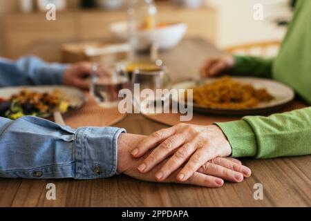 Senior woman stacking hand on man at dining table Stock Photo