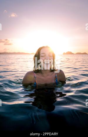 Happy woman with eyes closed swimming in sea at sunset Stock Photo