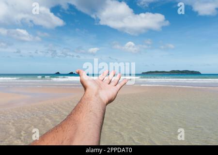 Man's hand reaching towards sea at beach Stock Photo