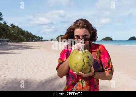 Smiling young woman drinking coconut water at beach Stock Photo