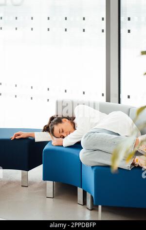 Tired young woman in lab coat lying on sofa Stock Photo