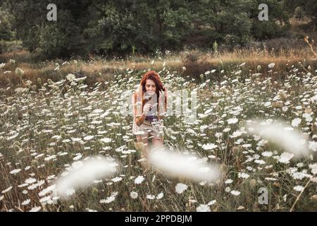 Redhead young woman smelling white flowers at field Stock Photo
