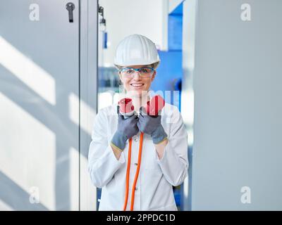 Happy woman wearing lab coat analyzing power plug in laboratory Stock Photo