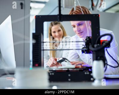 Engineer with colleague operating 3D printing machine in laboratory Stock Photo