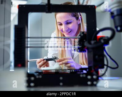 Smiling engineer holding vernier calliper operating 3D printing machine in laboratory Stock Photo