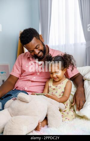 Father and daughter watching mobile phone sitting on bed in bedroom Stock Photo