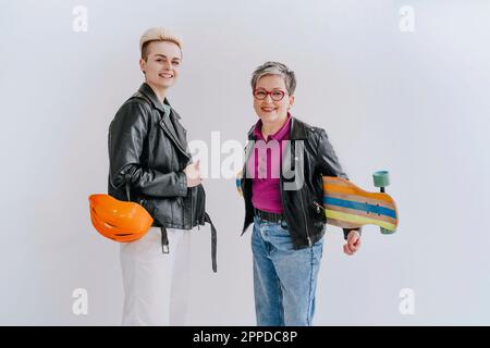 Happy young woman standing with mother holding skateboard in front of white wall Stock Photo