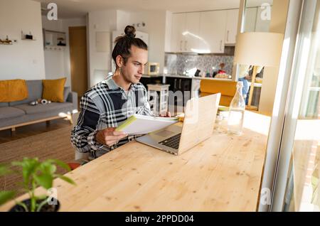Young man with document working on laptop at home office Stock Photo