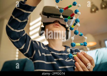 Boy examining DNA model through VR glasses at home Stock Photo
