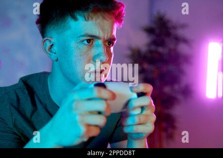 Young man concentrating with controller playing video game at home Stock Photo