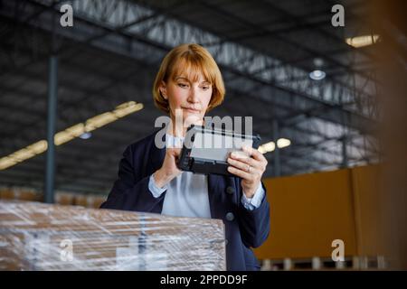 Manager using tablet PC standing by stocks in warehouse Stock Photo