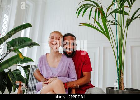 Happy man hugging woman sitting in armchair at home Stock Photo