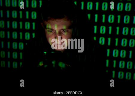 Young man wearing hood in front of binary numbers Stock Photo