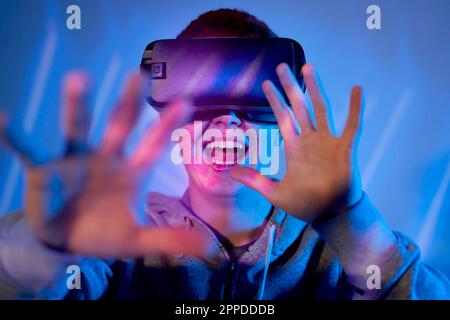 Happy man wearing VR glasses gesturing in front of wall Stock Photo