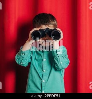 Boy looking through binoculars in front of curtain Stock Photo