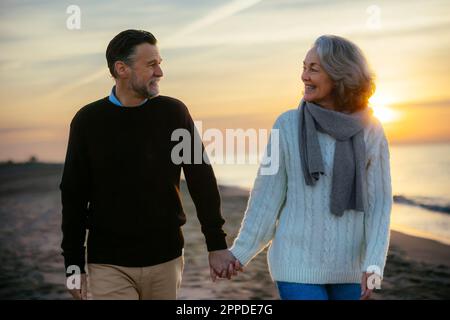 happy mature couple holding hands and walking at beach Stock Photo