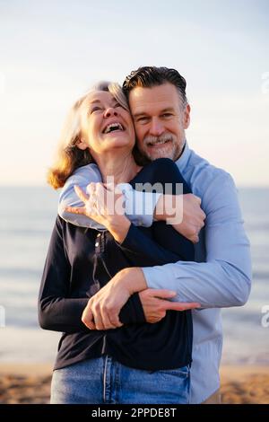 Happy man hugging cheerful mature woman at beach Stock Photo