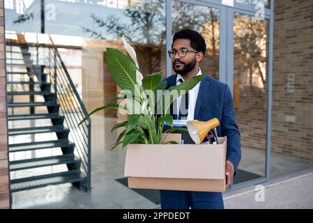 Thoughtful businessman carrying cardboard box leaving office building Stock Photo