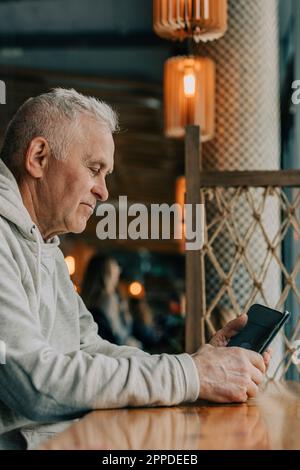 Senior man using smart phone sitting in cafe Stock Photo