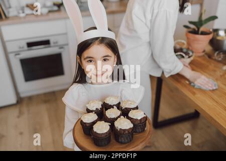 Smiling girl holding cupcakes on Easter day at home Stock Photo