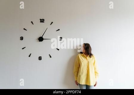 Woman looking at large clock on white wall Stock Photo