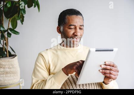 Man using tablet PC sitting in front of wall at home Stock Photo