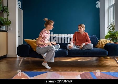 Mother and upset teenage daughter sitting on sofa having difficult conversation at home Stock Photo