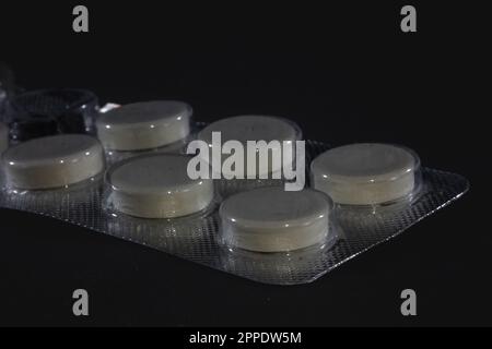 picture of a half empty blister pack of tablets, white pills, of pain killer medicine isolated on a black background. Stock Photo