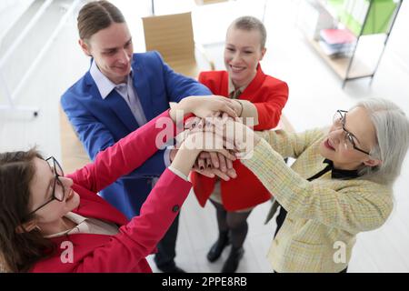 Smiling employees and boss joins hands in corporate office Stock Photo