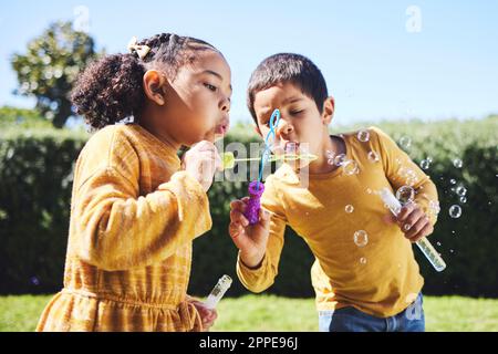 Playing, garden and children blowing bubbles for entertainment, weekend and fun activity together. Recreation, outdoors and siblings with a bubble toy Stock Photo