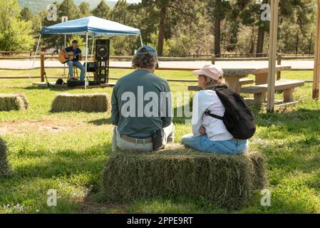 A man and woman sit on bales of hay listening to musician playing guitar during the Chama Valley Arts Festival in Chama, New Mexico, United States. Stock Photo