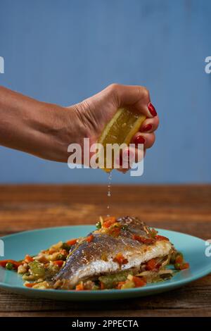 Grilled bream with vegetables on a blue plate on a wooden board Stock Photo