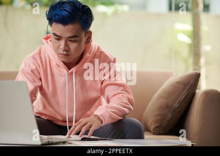 Serious young man studying online watching webinars on laptop and taking notes Stock Photo