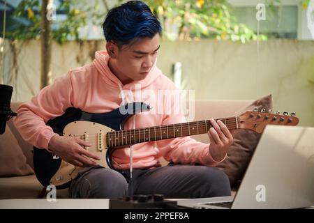 Portrait of young man concentrated on playing electric guitar and practising new chord Stock Photo