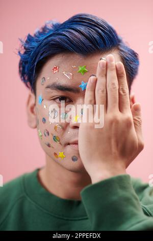 Young man with stickers on face covering half of face with hand Stock Photo