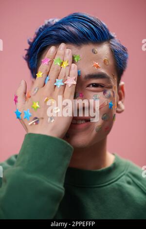 Creative smiling young man with bright stickers on face and hands looking at camera Stock Photo